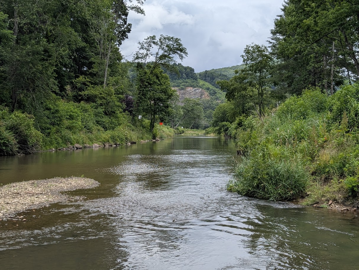 A river between tree-lined banks with a rocky hillside beyond.